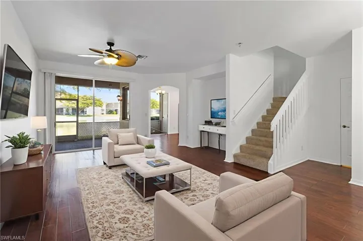 Living room featuring arched walkways, stairs, a ceiling fan, and dark wood-style flooring