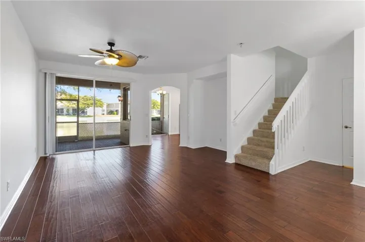 Unfurnished living room featuring dark wood-style floors, stairs, arched walkways, and a ceiling fan