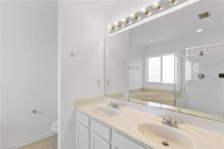 Full bath featuring a bath, light tile patterned flooring, a stall shower, and double vanity