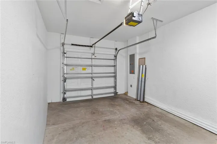 Garage with a textured wall, electric panel, and a garage door opener