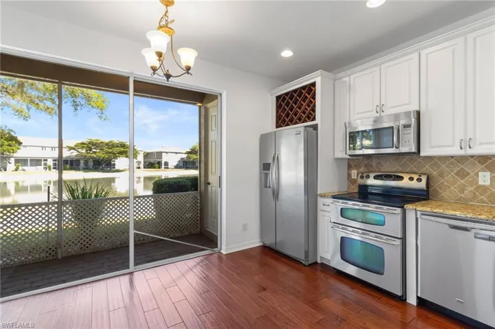 Kitchen featuring appliances with stainless steel finishes, white cabinets, hanging light fixtures, decorative backsplash, and light stone counters