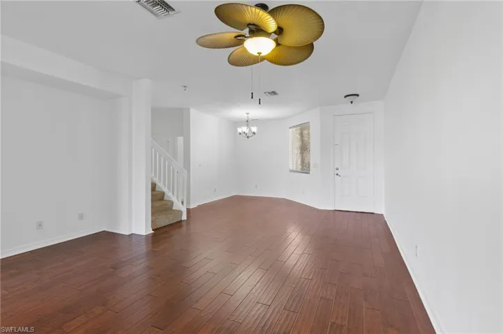 Unfurnished living room with dark wood-style floors, stairs, ceiling fan, and a chandelier