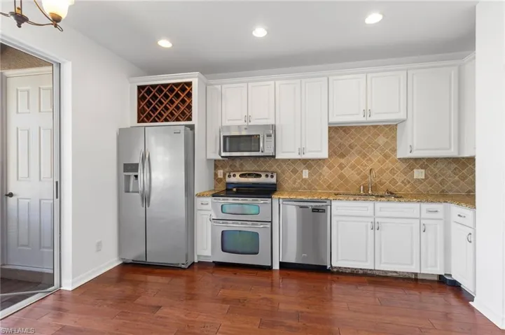 Kitchen with stainless steel appliances, light stone counters, white cabinets, backsplash, and dark wood finished floors