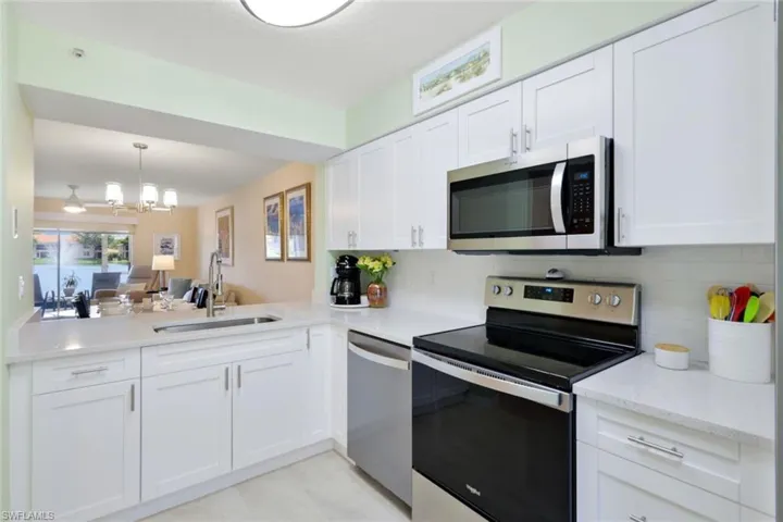 Kitchen with stainless steel appliances, an inviting chandelier, backsplash, sink, and white cabinetry