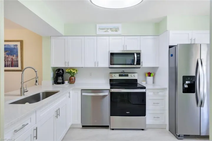 Kitchen with sink, stainless steel appliances, white cabinetry, and light tile floors