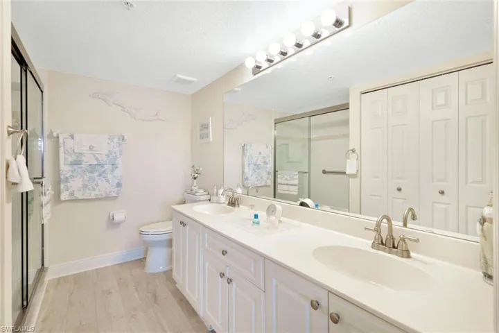 Bathroom featuring a shower with door, a textured ceiling, dual bowl vanity, hardwood / wood-style flooring, and toilet