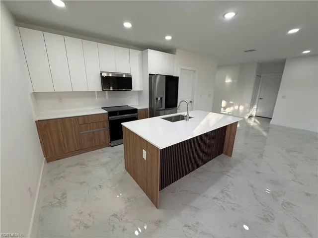 Two tone kitchen with modern cabinets, dual tone cabinetry, stainless steel appliances, recessed lighting, and a kitchen island with sink