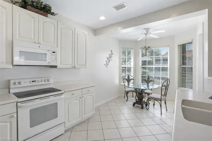 Kitchen with white appliances, light countertops, light tile patterned floors, white cabinets, and ceiling fan