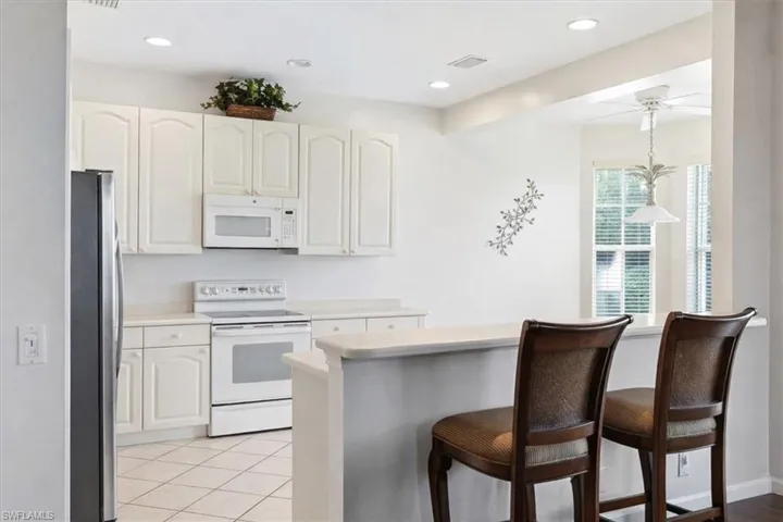 Kitchen with white appliances, a kitchen bar, light countertops, and white cabinets
