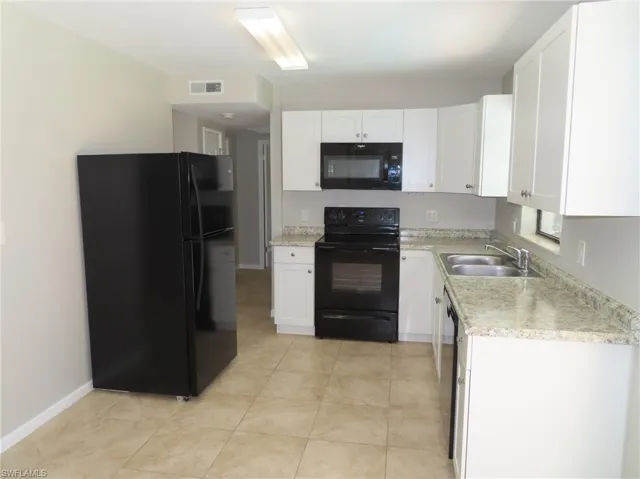 Kitchen featuring black appliances, white cabinets, light stone counters, sink, and light tile flooring