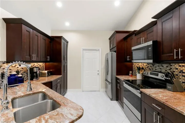 Kitchen with stainless steel appliances, backsplash, light stone countertops, dark brown cabinetry, and recessed lighting