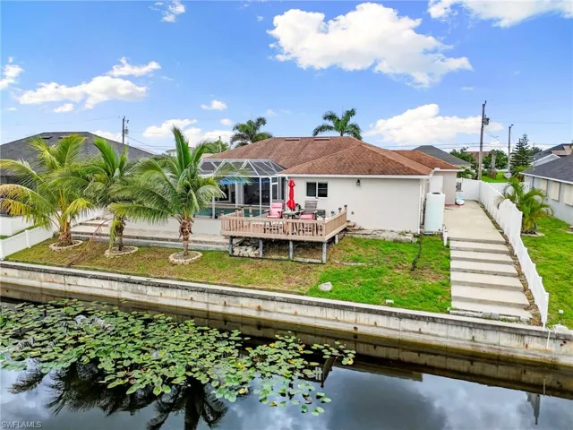 Rear view of property with a water view, glass enclosure, a fenced backyard, and stucco siding