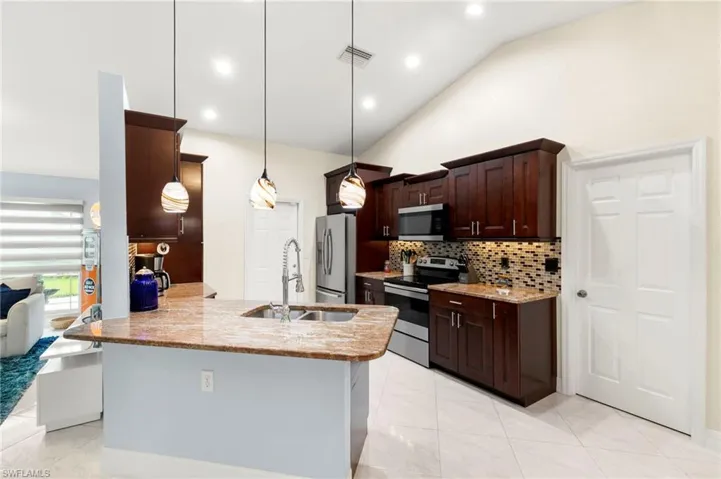 Kitchen featuring vaulted ceiling, appliances with stainless steel finishes, dark brown cabinetry, recessed lighting, and backsplash