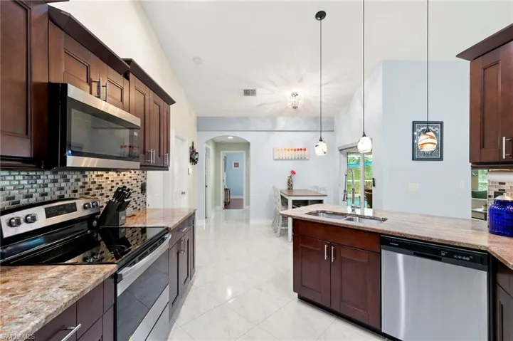 Kitchen with tasteful backsplash, appliances with stainless steel finishes, arched walkways, and dark brown cabinetry