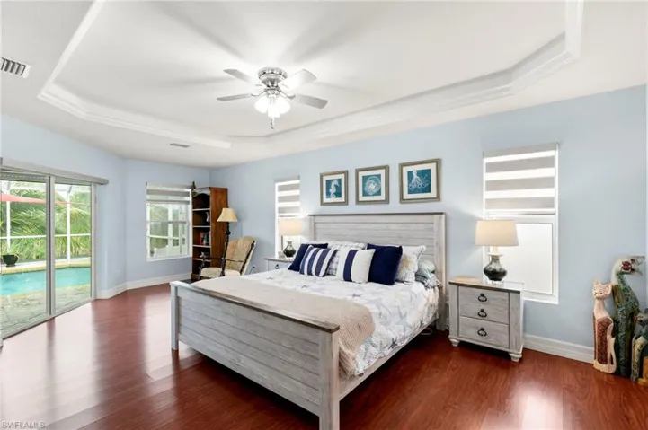 Bedroom with a tray ceiling, access to exterior, wood finished floors, a ceiling fan, and ornamental molding