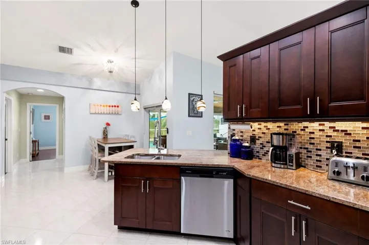 Kitchen featuring a peninsula, dishwasher, arched walkways, light stone counters, and decorative backsplash