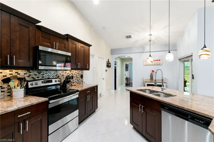 Kitchen with stainless steel appliances, arched walkways, light stone counters, and pendant lighting