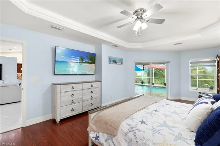 Bedroom with a raised ceiling, access to exterior, wood finished floors, a ceiling fan, and crown molding