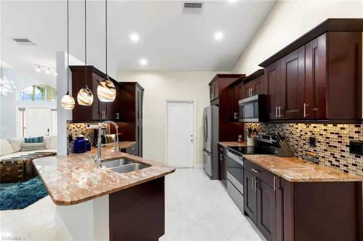 Kitchen with backsplash, appliances with stainless steel finishes, light stone countertops, vaulted ceiling, and dark brown cabinetry