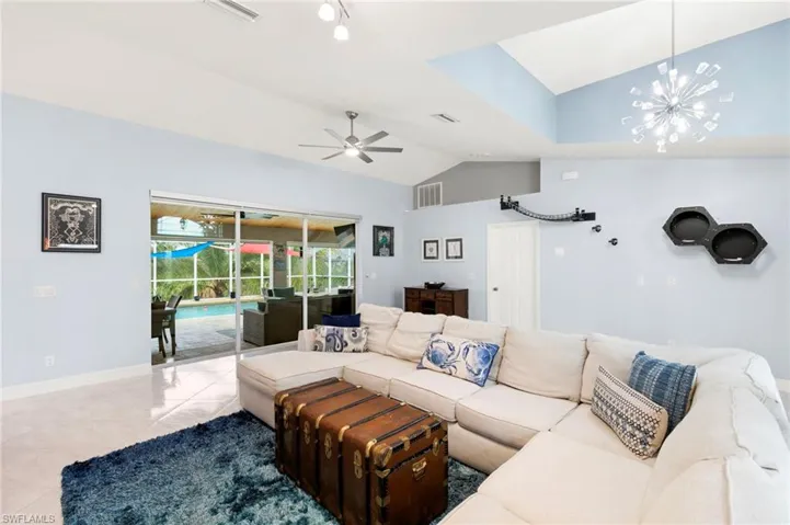 Living room with vaulted ceiling, light tile patterned flooring, a ceiling fan, and a chandelier