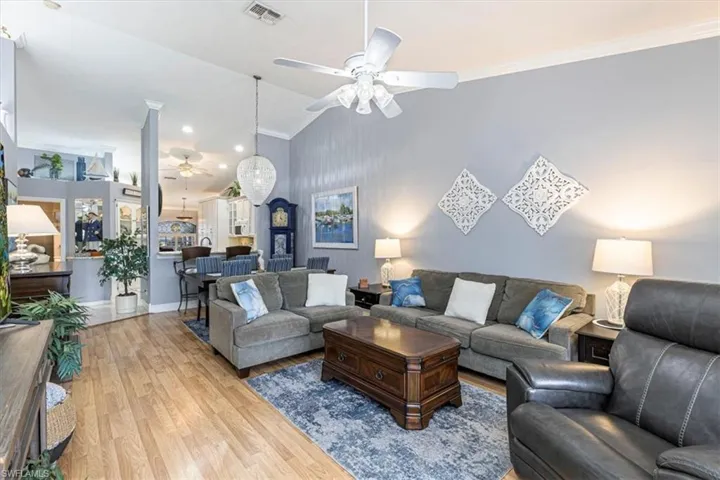 Living room featuring an accent wall, wood finished floors, lofted ceiling, crown molding & ceiling fan.