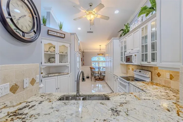 Kitchen featuring glass insert cabinets, white cabinets, crown molding, tasteful backsplash & white appliances.