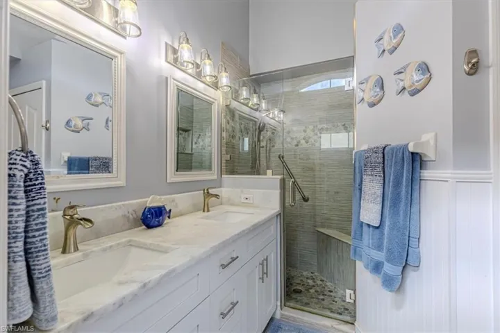 Primary bathroom featuring double vanity, a stall shower & wainscoting.