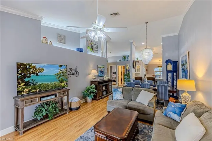 Living room featuring ornamental molding, ceiling fan, wood finished floors, chandelier & recessed lighting.