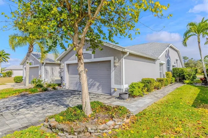 View of side of home featuring an attached 2 car garage, decorative paver driveway, a yard, stucco siding, and roof with shingles.