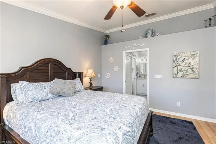 Primary Bedroom featuring ornamental molding, ensuite bath, ceiling fan & wood finished floors.