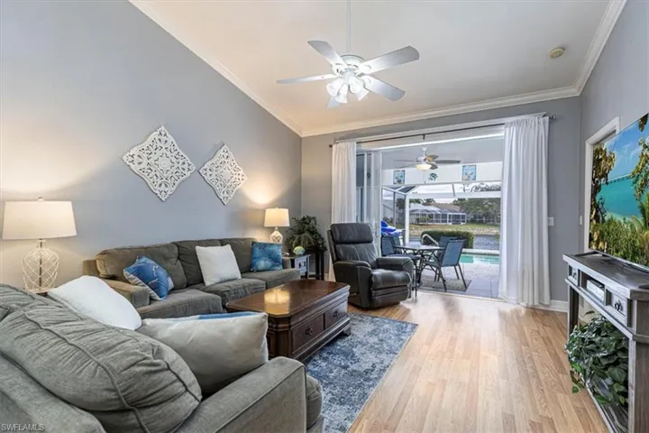 Living room featuring wood finished floors, a ceiling fan & crown molding.