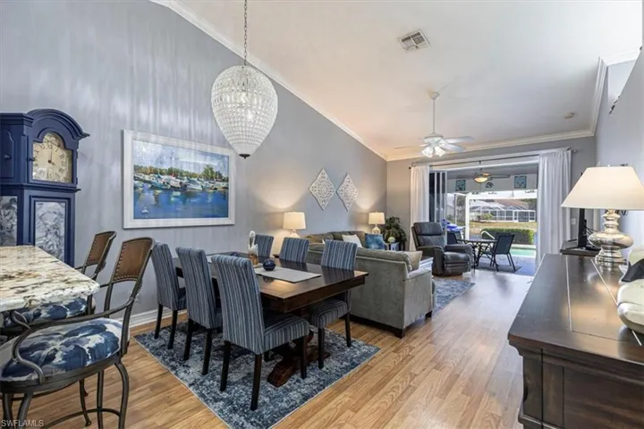 Dining room featuring a chandelier, light wood finished floors, ceiling fan, ornamental molding, vaulted ceiling.