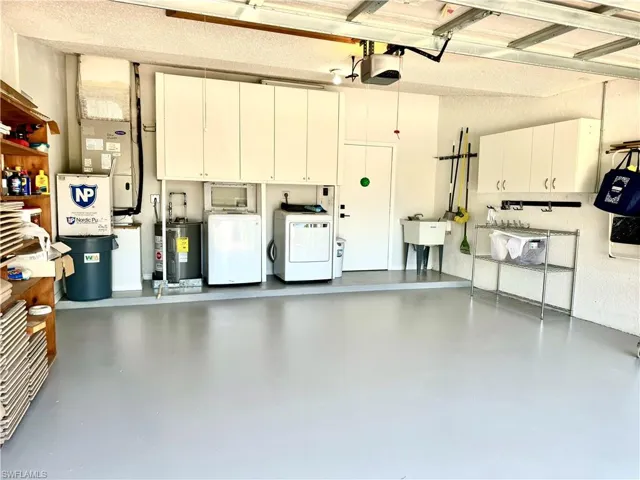 Garage with a garage door opener, water heater, separate washer and dryer, and sink