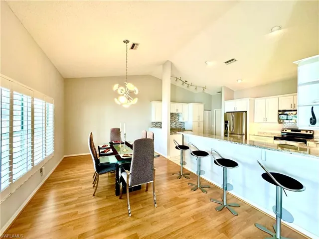 Dining area with light hardwood / wood-style floors, a chandelier, and high vaulted ceiling