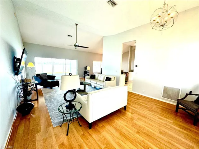 Living room featuring ceiling fan with notable chandelier and wood-type flooring