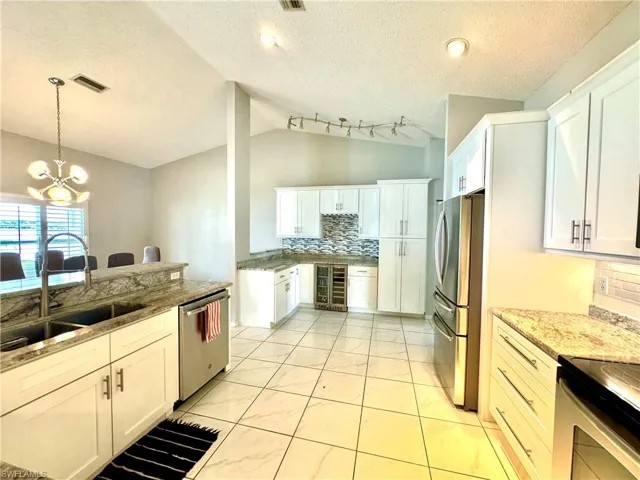 Kitchen featuring white cabinets, wine cooler, sink, an inviting chandelier, and vaulted ceiling