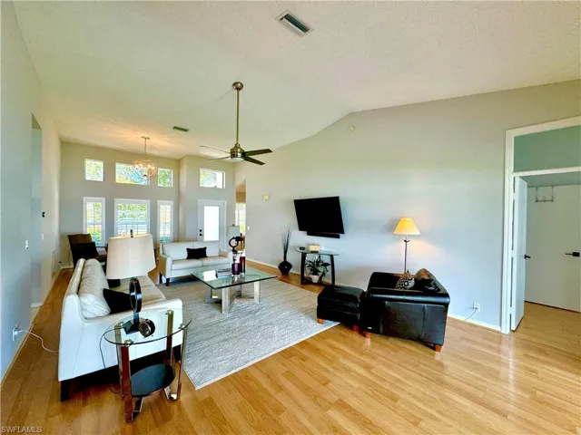 Living room with ceiling fan with notable chandelier, light wood-type flooring, vaulted ceiling, and a textured ceiling