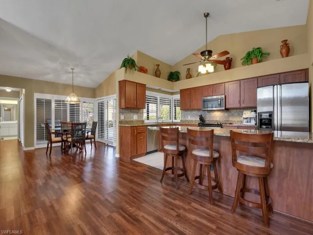 Kitchen with tasteful backsplash, appliances with stainless steel finishes, dark wood-type flooring, and light stone counters