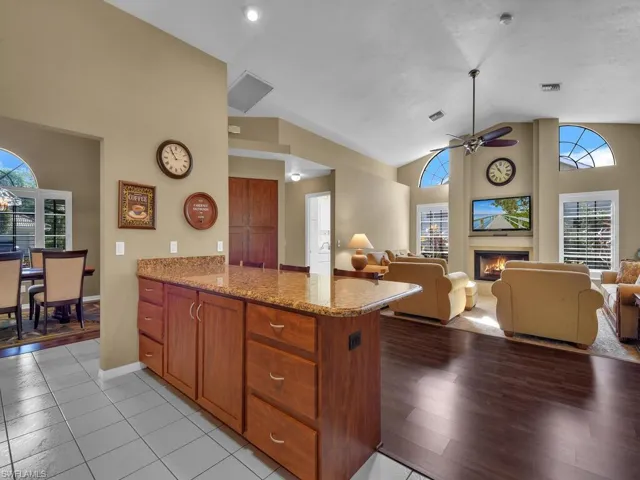 Kitchen featuring ceiling fan, high vaulted ceiling, light stone countertops, kitchen peninsula, and light wood-type flooring