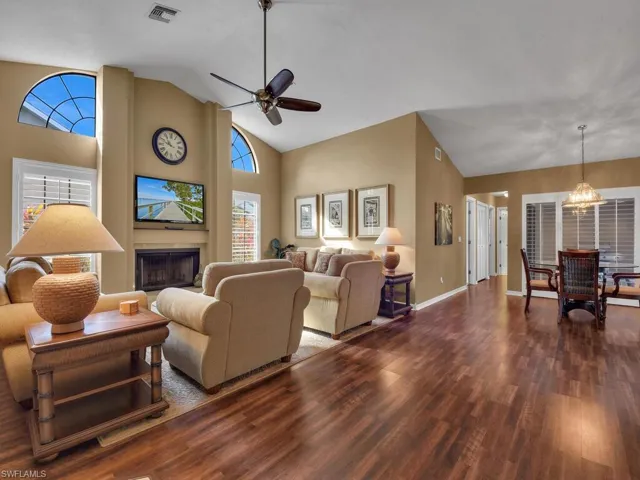 Living room featuring high vaulted ceiling, a large fireplace, ceiling fan with notable chandelier, and dark hardwood / wood-style flooring
