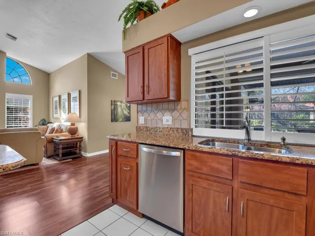 Kitchen featuring sink, light tile patterned floors, light stone counters, decorative backsplash, and stainless steel dishwasher