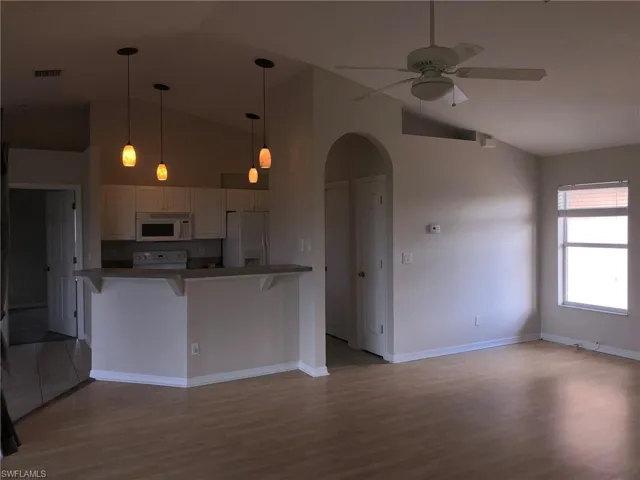 Kitchen featuring arched walkways, a breakfast bar, vaulted ceiling, white appliances, and ceiling fan