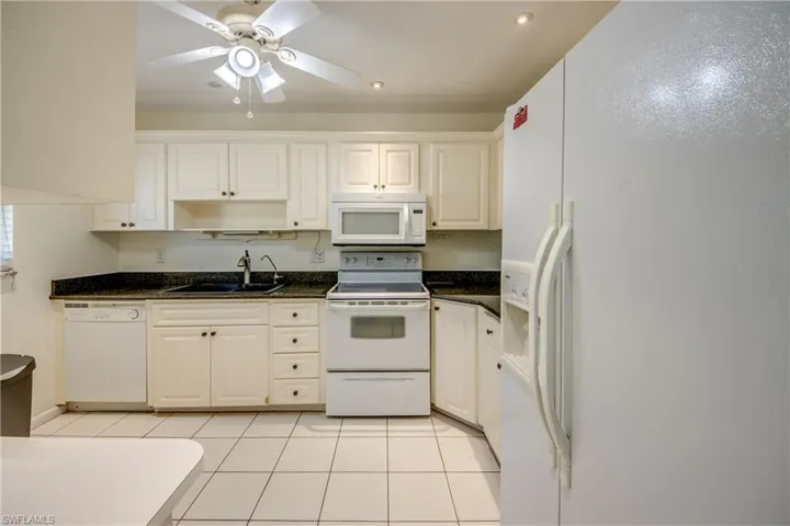 Kitchen featuring white cabinetry, sink, ceiling fan, light tile patterned floors, and white appliances