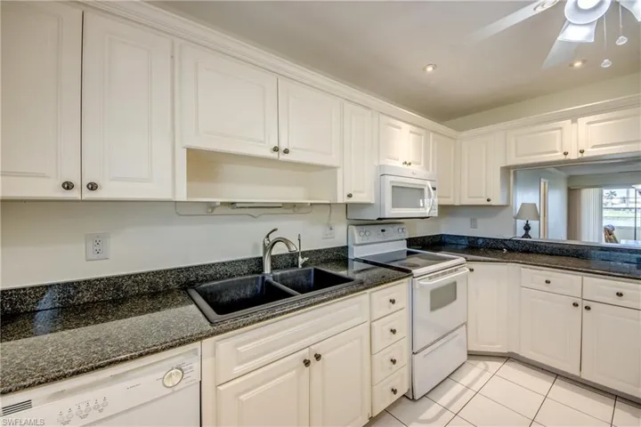 Kitchen featuring white appliances, dark stone countertops, white cabinetry, and sink