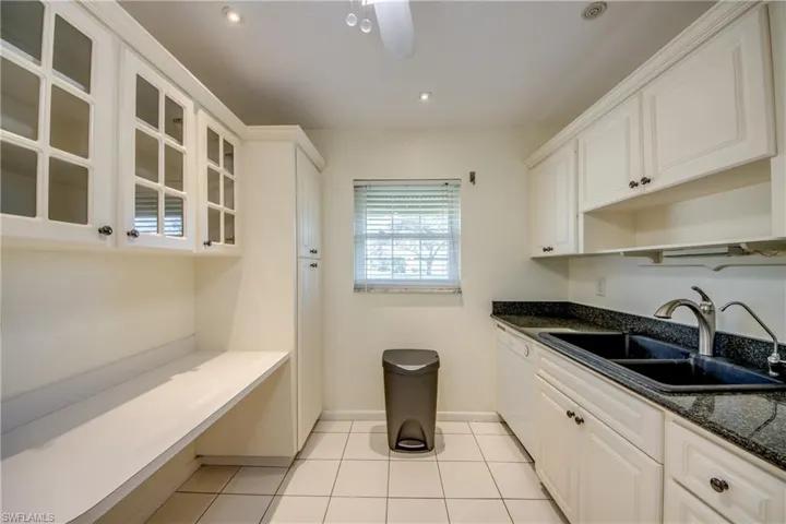 Kitchen featuring dark stone countertops, sink, light tile patterned floors, and white cabinets