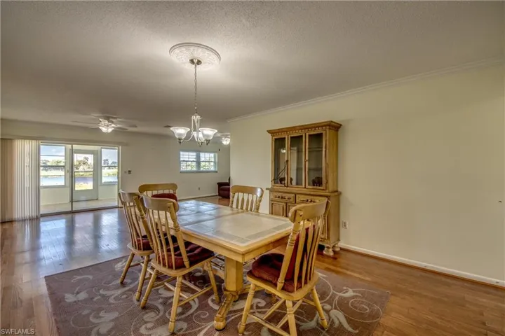 Dining room with ceiling fan with notable chandelier, a healthy amount of sunlight, a textured ceiling, and dark hardwood / wood-style flooring
