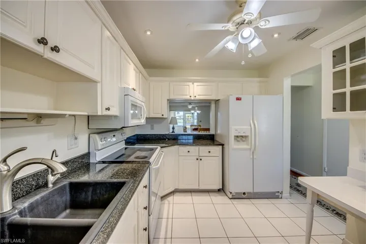 Kitchen with sink, light tile patterned floors, ceiling fan, white cabinetry, and white appliances