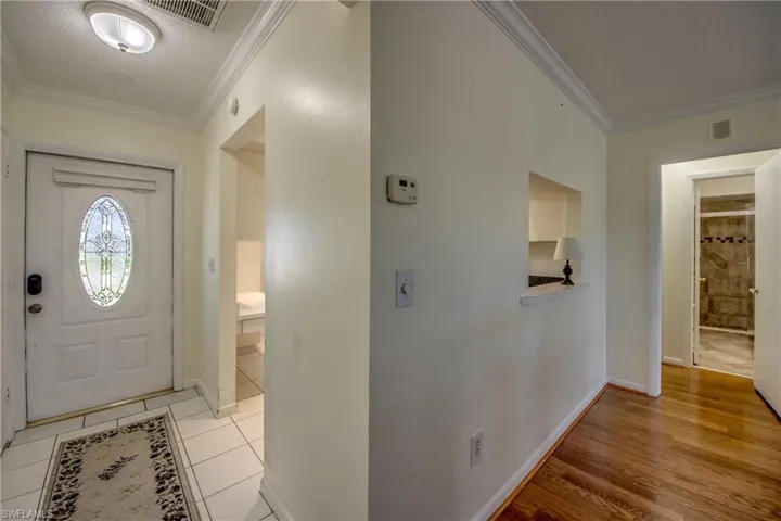 Foyer entrance with a textured ceiling, light tile patterned floors, and crown molding