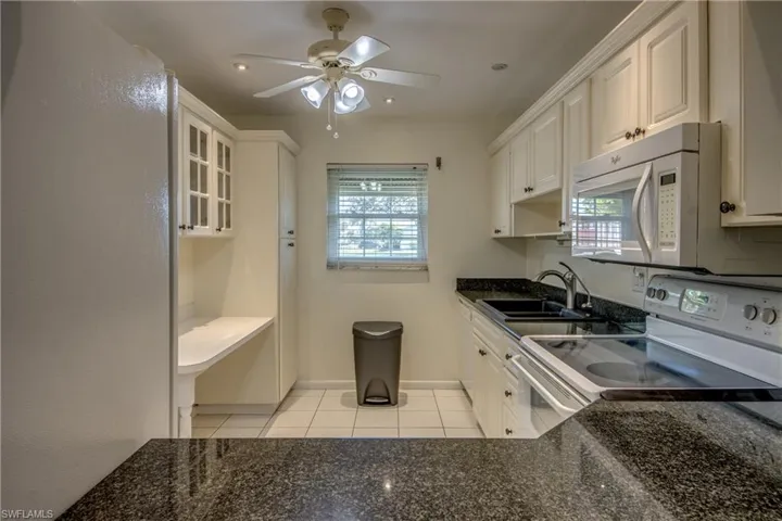 Kitchen with sink, light tile patterned floors, white cabinetry, white appliances, and dark stone countertops