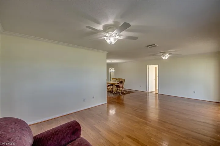 Living room featuring ceiling fan with notable chandelier, a textured ceiling, light wood-type flooring, and ornamental molding